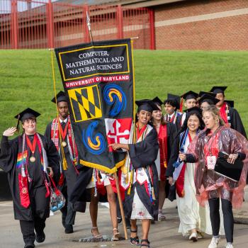 A group of graduates wearing regalia carrying gonfalon into commencement