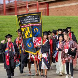 A group of graduates wearing regalia carrying gonfalon into commencement